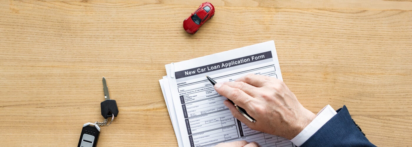 overhead view of someone filling out a new car loan application form and a key on the desk